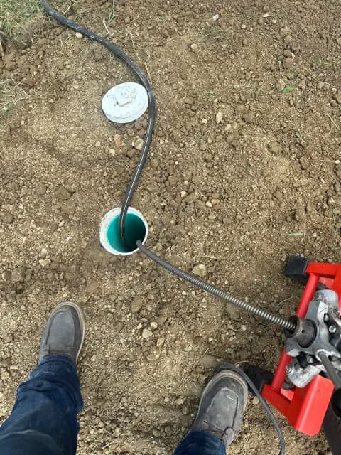 Drain machine cable running into an exterior sewer cleanout in soil