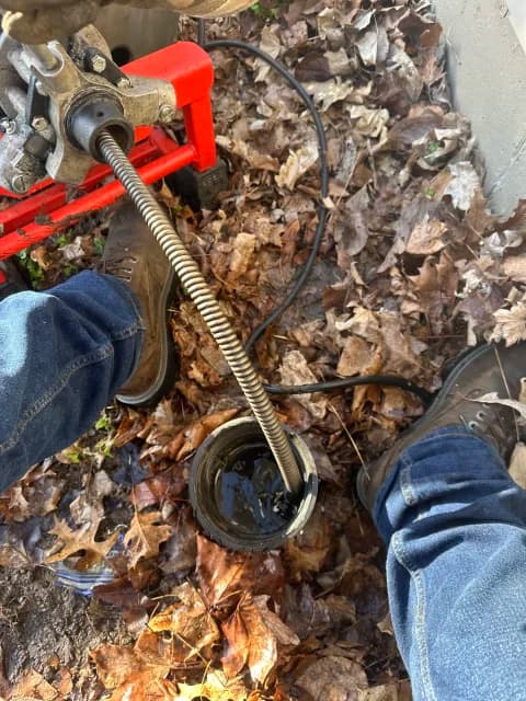 Drain machine cable clearing a clogged exterior cleanout beside a foundation
