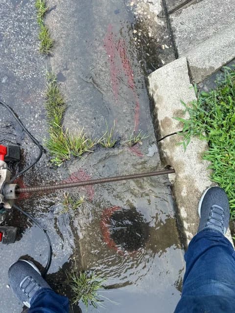 Storm drain cable cleaning at a curb line with standing water in the gutter