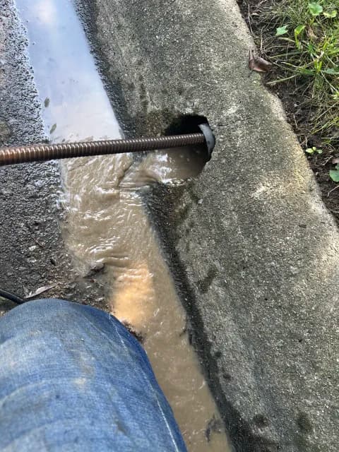 Clearing a clogged curb drain with muddy water flowing from the opening